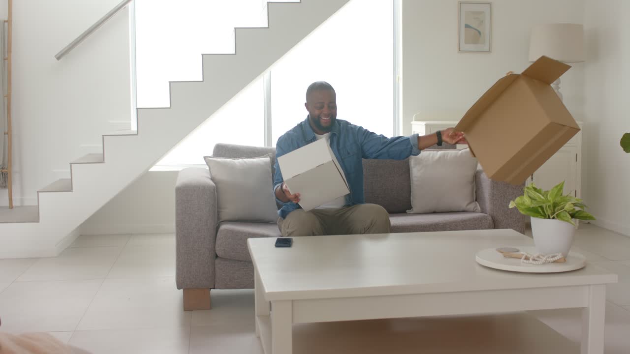 African American man in blue shirt noticing brown box, opening inspecting white box in living room