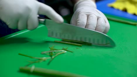 las manos del chef cortando cebolla verde en la tabla de cortar verde, de cerca