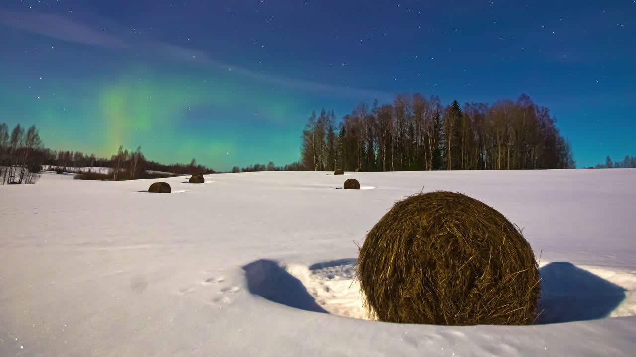 Aikaerokuva revontulista, pohjoisista valoista ja tähdistä lumisen maaseutumaiseman yllä.
