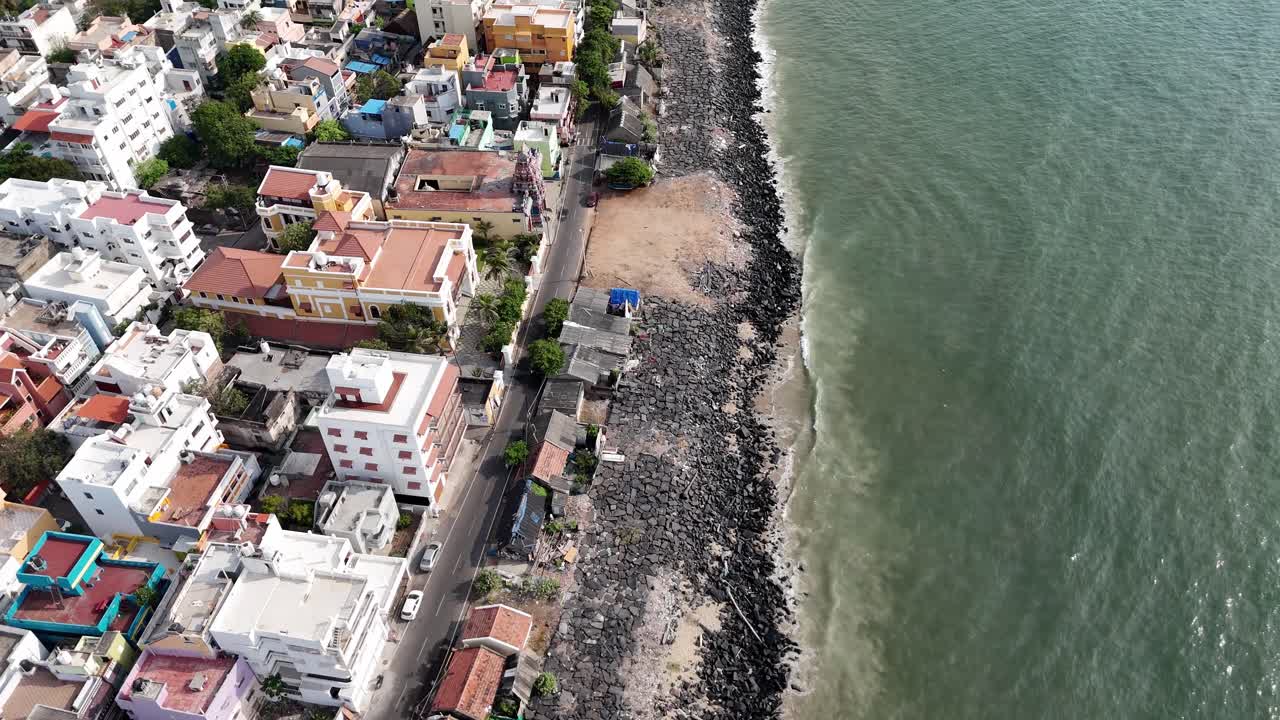 A picturesque blend of urban life and natural beauty. This drone shot shows a city's shoreline, with a promenade and buildings stretching along the calm, grey ocean. Fishing town