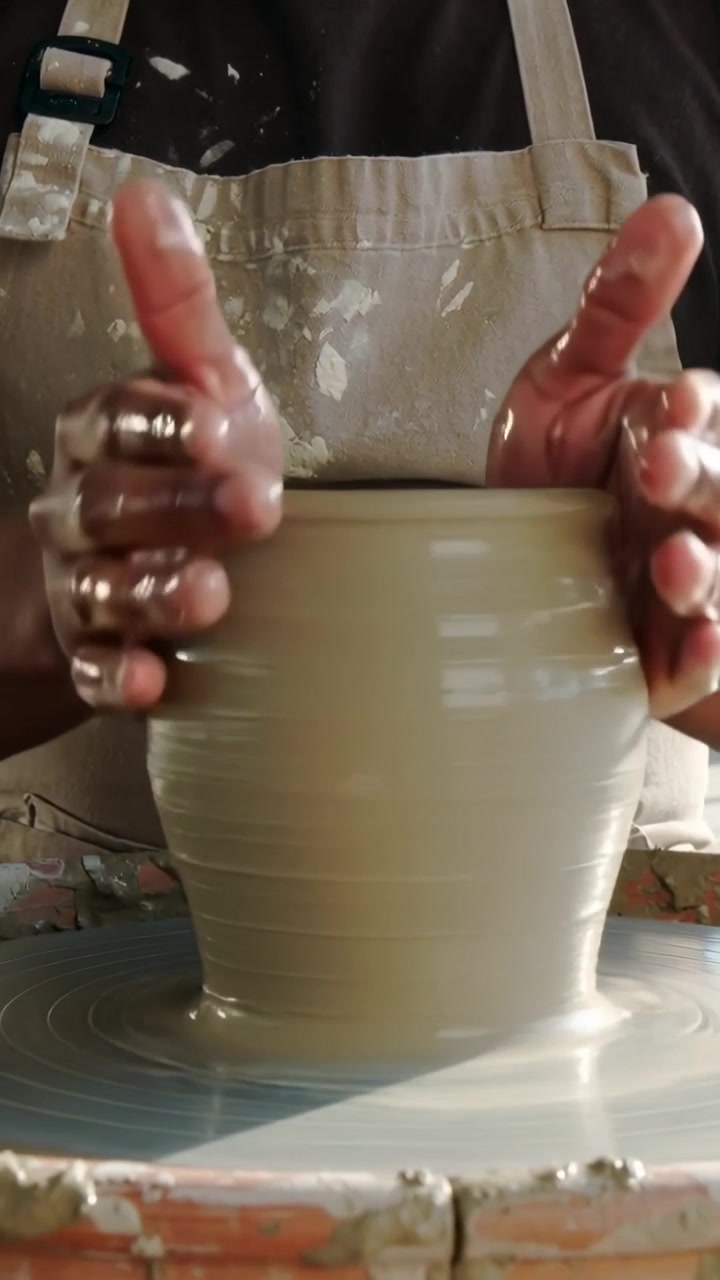 Video verticale: La ruota che inizia a girare, vasaio che modella l'argilla in un vaso in studio, con il grembiule macchiato.