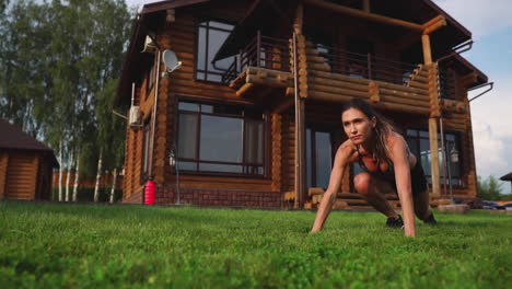 A-slender-young-woman-in-black-sportswear-performs-squats-on-the-grass-near-her-country-house