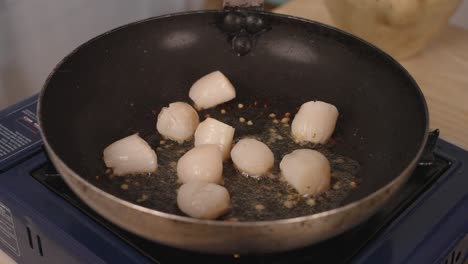 pan frying fresh seafood scallops with garlic, oil popping and splattering, close up shot of home cook meal food preparation