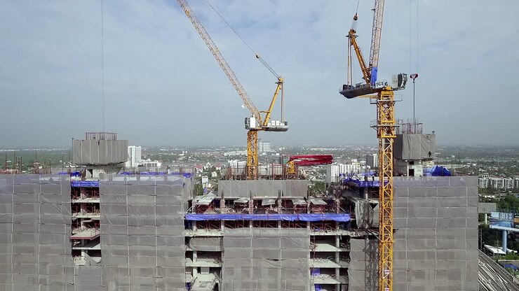 Aerial view of a building construction site with workers assembling the structural framework, machinery in operation, and materials arranged across the work area in an active urban project