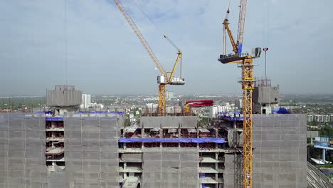 aerial view of a building construction site with workers assembling the structural framework, machinery in operation, and materials arranged across the work area in an active urban project
