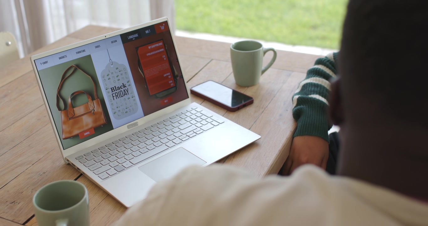 Camera is shifting as two adults are browsing Black Friday deals on laptop at wooden table
