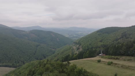 an aerial shot begins with the treetops in the foreground. as the drone ascends, it reveals rolling green mountain ranges in the distance.