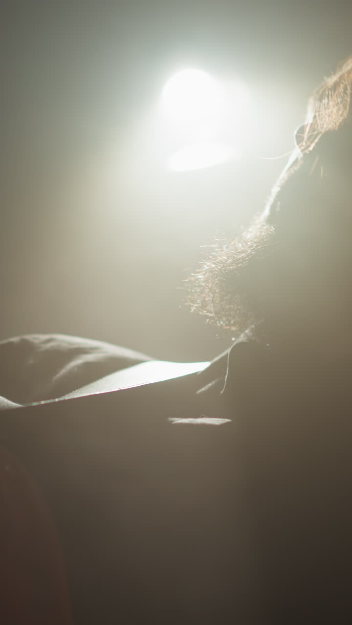 검은 옷을 입은 수염이 있는 기타리스트가 어두운 방에서 스포트라이트 아래 은 기타를 연주하고 있습니다.