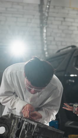 dos inventores en un taller automotriz chino, un niño le muestra la lectura a una niña mientras ella graba datos en una tableta, mide el componente del motor de nuevo bajo una escena de iluminación de luz brillante