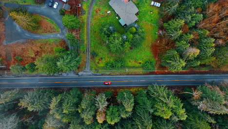 red car drives by the highway in the beautiful countryside. footage from drone on the lovely nature alongside with lonely cottages in wilderness.