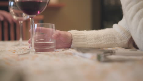 woman's hand holding glass with water at the table during family lunch at home - close up, static shot