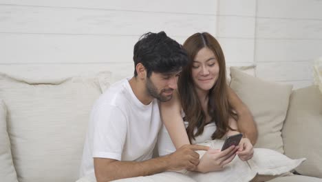 행복한 중동 젊은 남성과 아시아 여성, 소셜 미디어에서 스마트폰을 사용하는 사람들, 집에서 사파에 앉아있는 사람들, 기술 장치의 라이프 스타일, 다민족