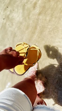 holding sandals while entering clear beach water barefoot