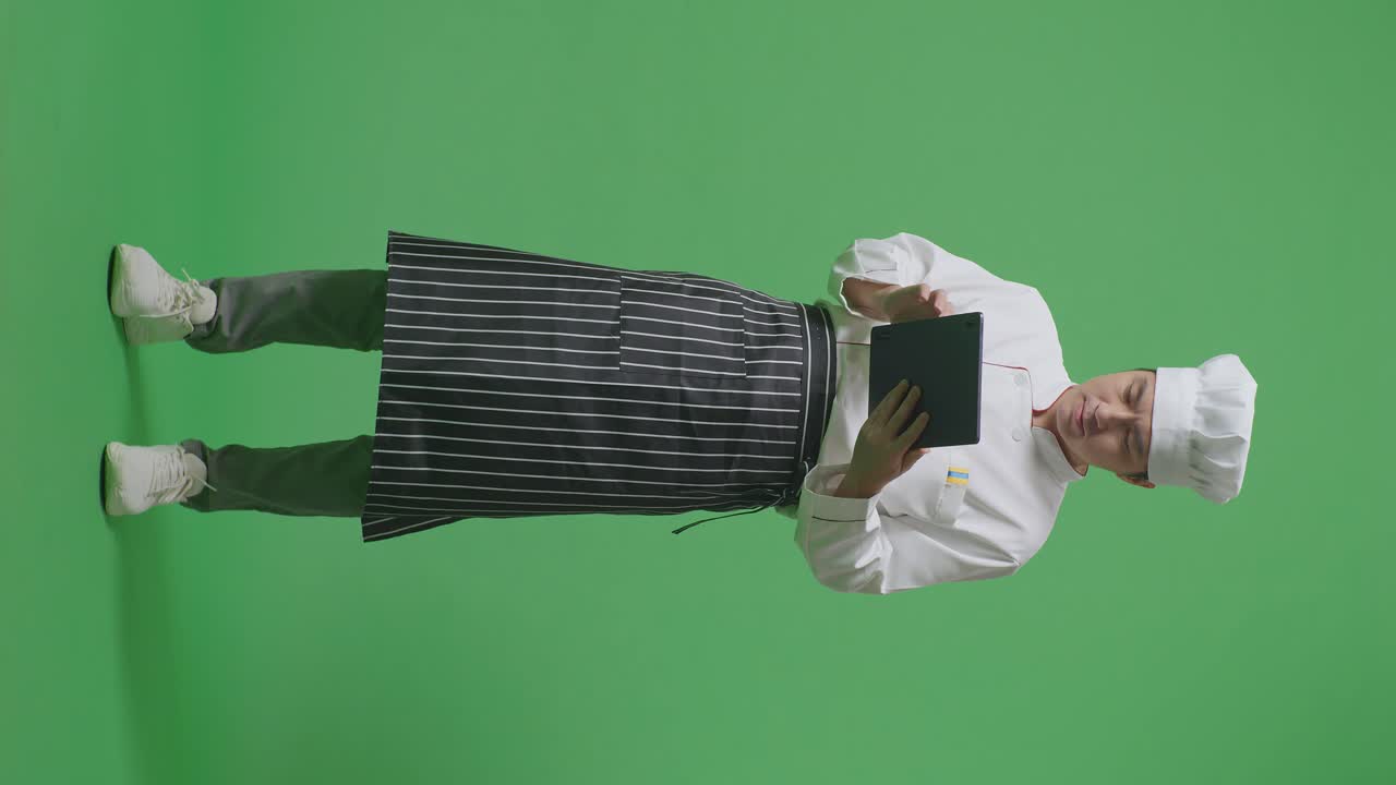 cuerpo lleno de cocinero hombre asiático usando una tableta mientras estaba de pie en el estudio de fondo de la pantalla verde