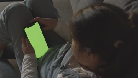 young girl at home relaxing on sofa looking at green screen mobile phone 1