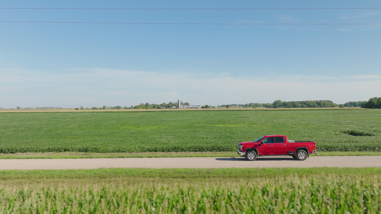 정오에 농장 근처의 시골 도로에서 운전하는 빨간 픽업 트럭