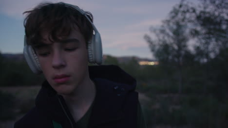 teenager walking through rural landscape at dusk, listening to wireless headphones, expressing various emotions and gestures while enjoying personal moment of tranquility