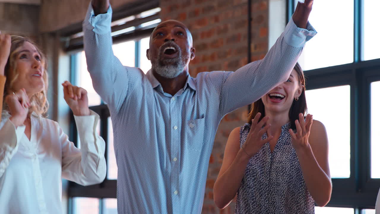 Business Team Celebrating In Multi-Cultural Office With Colleagues Throwing Paperwork In The Air