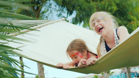 Zwei-Süße-Lustige-Schwestern-Mit-Bemalten-Gesichtern-Ruhen-Auf-Einer-Hängematte-Viel-Spaß-Beim-Lachen-Am-Meer-Mit-Der-Familie