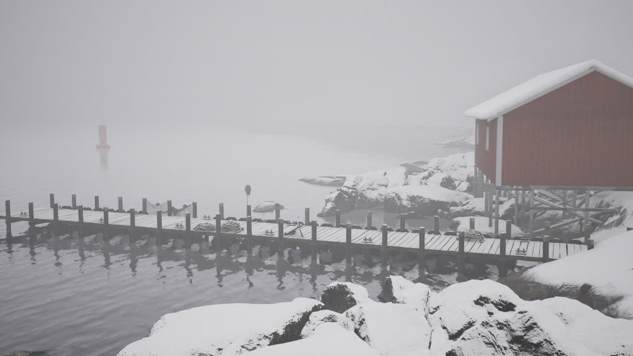 Snowy pier with a red house in foggy winter landscape near water