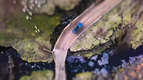 aerial view of a blue truck on a dirt road crossing a stream