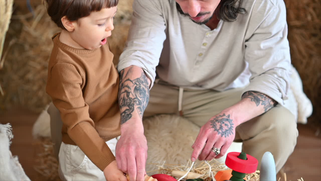 Padre jugando con su hijo con juguetes de madera ecológicos y coloridos en un granero, cerca de balas de heno cuadradas.