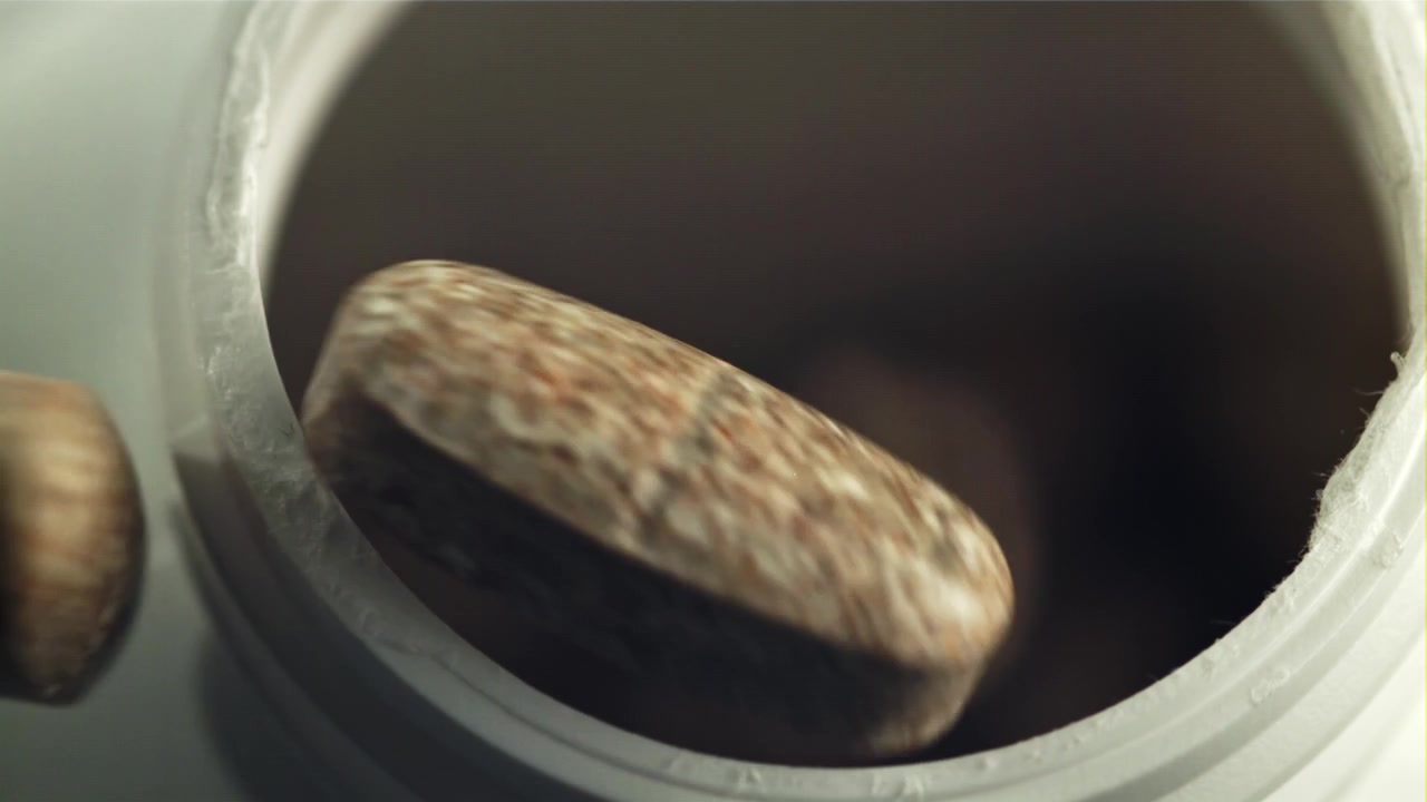 スローモーションで茶色の錠剤が白い容器に落ちる様子