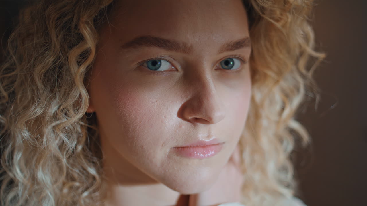 Serene woman looking camera in sunlight. Portrait curly girl touching