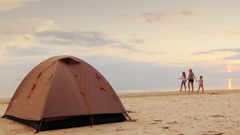 una mujer con sus dos hijas caminando por la orilla del mar en primer plano es una carpa para pasar la noche