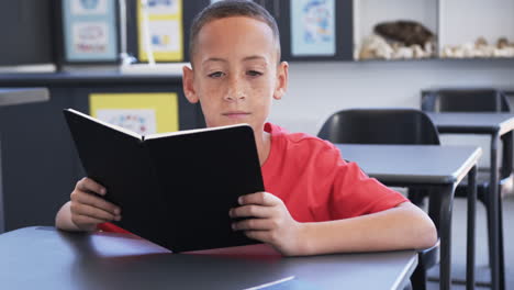 un niño biracial con pecas está leyendo un libro en un aula de la escuela