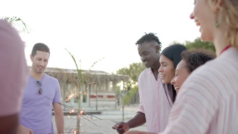 Happy-diverse-group-of-friends-burning-sparklers-in-circle-at-beach