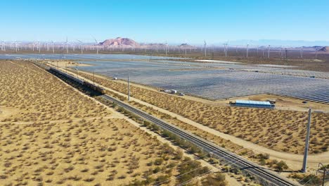 drone aerial of a freight train traveling through vast solar and wind array in mojave desert california