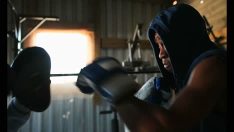 African-American-male-boxer-practicing-boxing-with-trainer-in-fitness-studio-4k