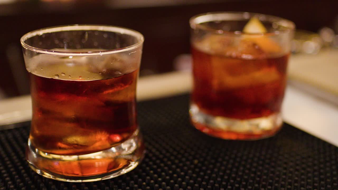 Bartender pours whiskey cocktail over ice in glass, warm ambient lighting, shallow depth of field