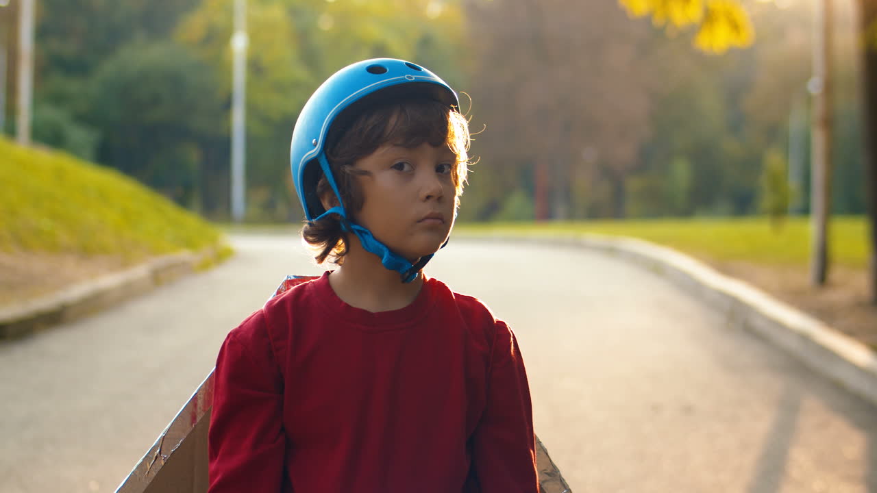 Portrait Of A Cute Little Boy In Helmet And Red Sweater Looking At The Camera While Standing In The Park On A Sunny Day