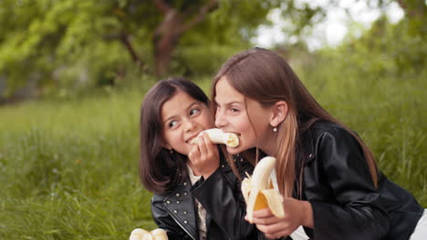 dos chicas comiendo plátanos en un parque