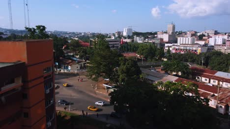 Flying-low-between-buildings-over-traffic-on-urban-streets-in-Yaounde-city,-sunny-Cameroon