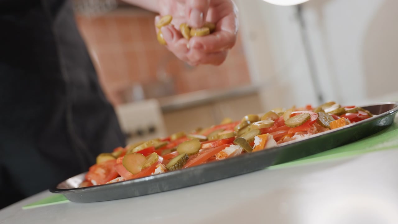 Vista ravvicinata di una mano che sparge erbe aromatiche su una pizza appena sfornata in una teglia di metallo in una cucina calda, con il condimento che cade, crosta dorata, formaggio fuso e un leggero movimento delle dita.