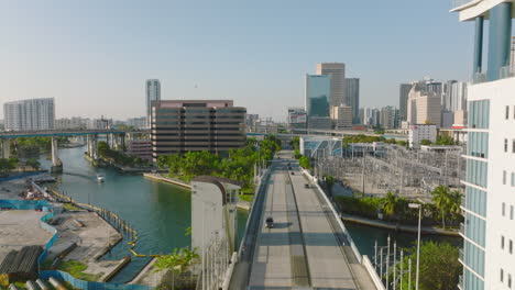 Forwards-tracking-of-cars-driving-on-street,-leading-over-bridge-and-along-electrical-substation-in-city.-Miami,-USA