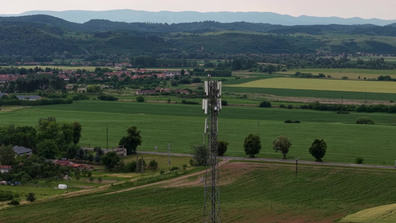 Un'alta torre cellulare si erge in modo prominente in un vasto e verde paesaggio rurale, simboleggiando la comunicazione moderna.