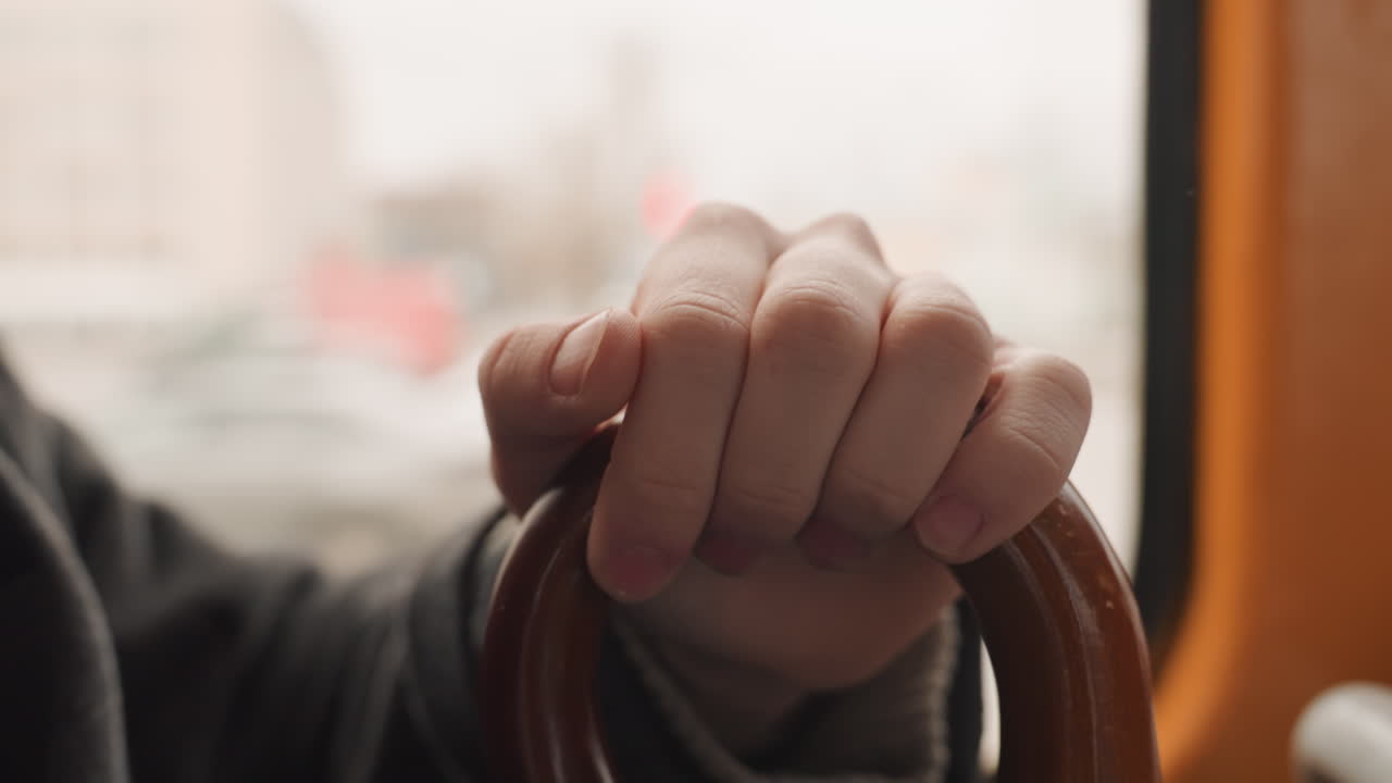 Persona che afferra un bastone attraverso il finestrino. Vista dettagliata di una mano che afferra un bastone vicino al finestrino con sfondo cittadino. Scatto intimo di una mano che tiene un bastone attraverso il finestrino di un autobus con uno sfondo urbano sfocato