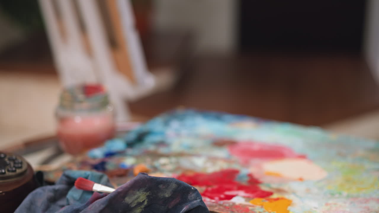 아티스트는 스튜디오 클로즈업에서 둥근 테이블에 컬러 팔레트를 놓습니다. 남자는 상점에서 오일 페인트 색소와 함께 나무 보드를 남니다. 예술 제조에 대한 공급