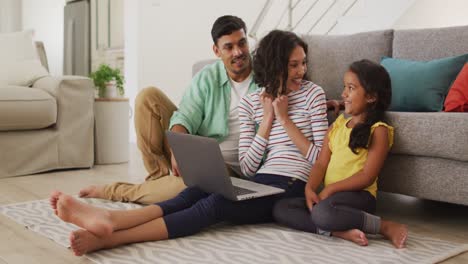 Happy-hispanic-parents-and-daughter-sitting-on-floor-using-laptop