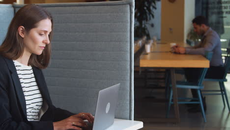 businesswoman at desk in cubicle in modern office work space using laptop