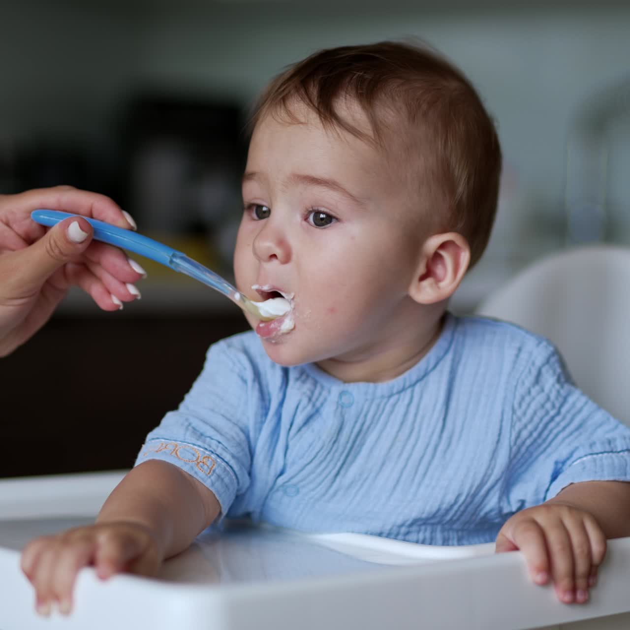 Adorable little child being fed from spoon. Cute nice baby takes the food and makes funny face. Close up