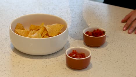 hands adding salsa to nachos in a bowl