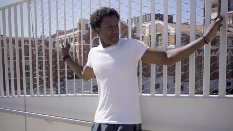 tired african american sportsman leaning on white metal fence.