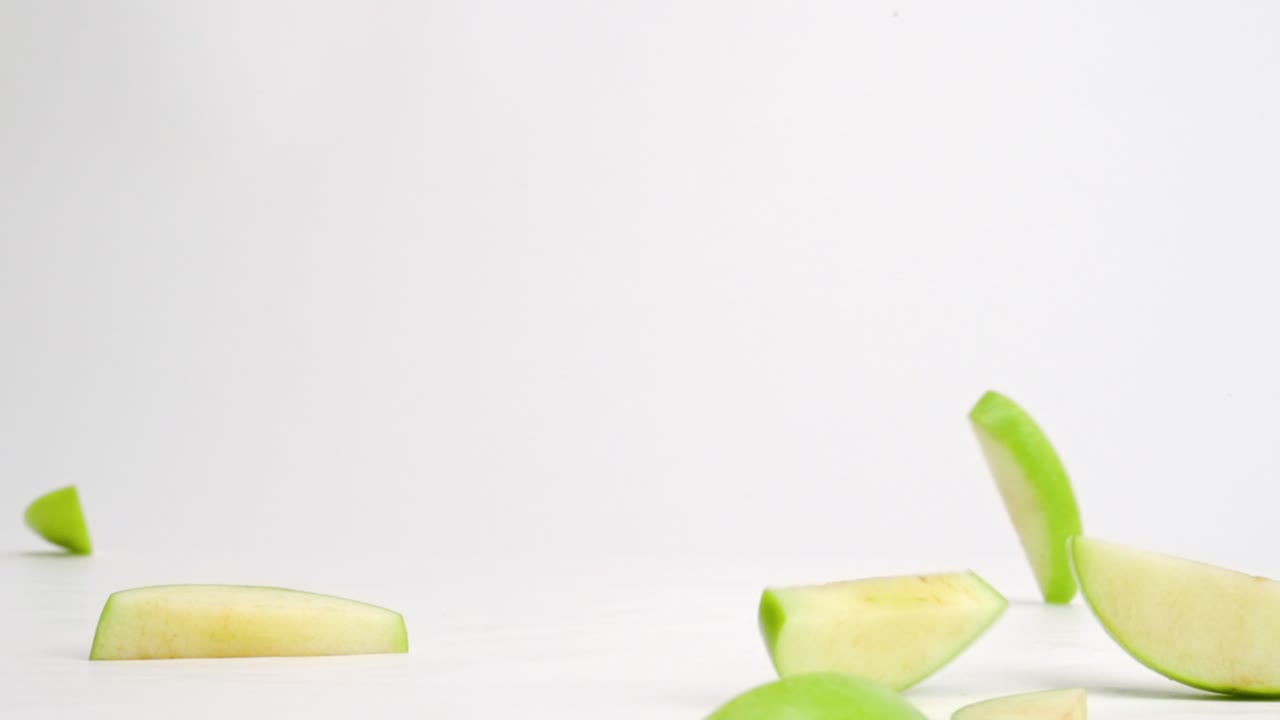 cortar rodajas de manzana verde aterrizando en la mesa blanca y rebotando en todas las direcciones en cámara lenta
