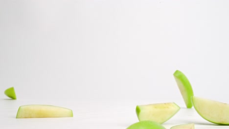 cut up green apple slices landing on white table top and bouncing in all directions in slow motion