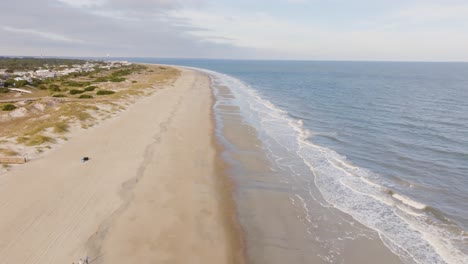 drone of an empty beach in tybee island approaching shops during warm sunny day with waves crashing